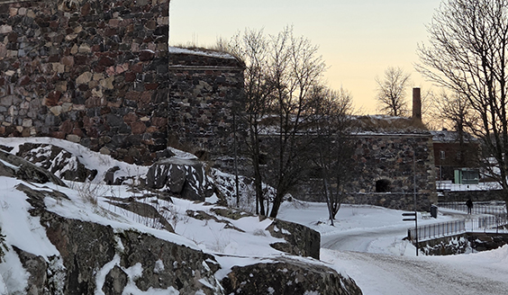Talvinen kuva Suomenlinnasta. Lumen peittämiä kallioita sekä linnoitusmuureja.